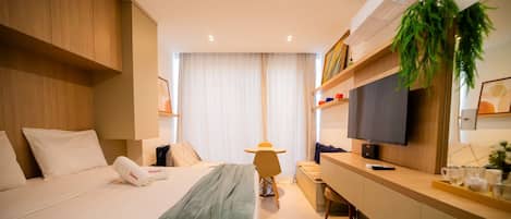 A hotel room with a bed, bedside table, TV, and a desk with a chair.