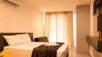 A hotel room with a bed, a chair, a desk, and a window with curtains.