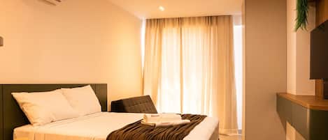 A hotel room with a bed, a chair, a desk, and a window with curtains.