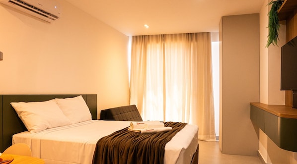 Una habitación de hotel con cama, una silla, escritorio y ventana con cortinas.