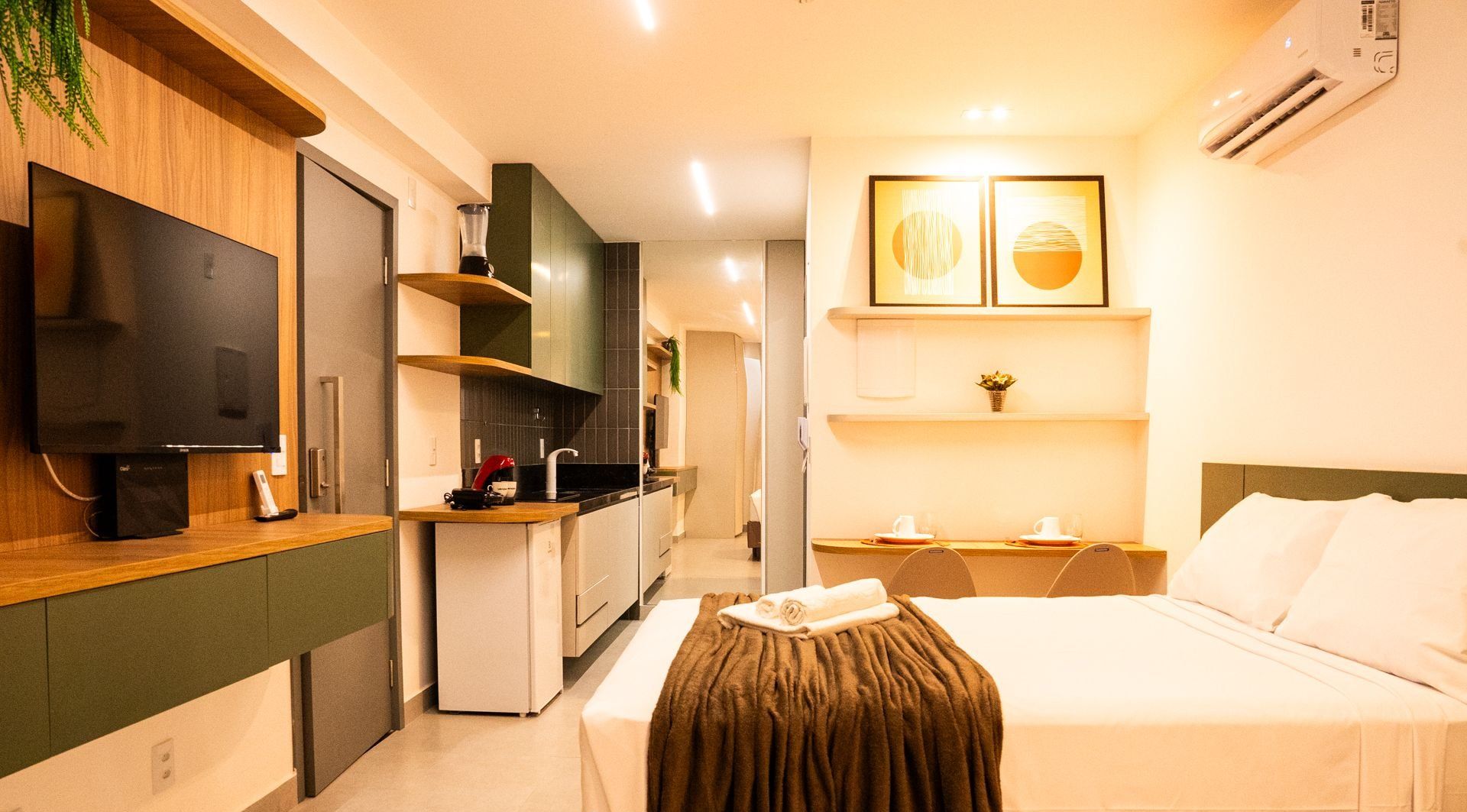 A hotel room with a bed, a TV, a kitchenette, and a small dining area.