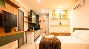 Una habitación de hotel con una cama, televisión, kitchenette y un pequeño comedor.