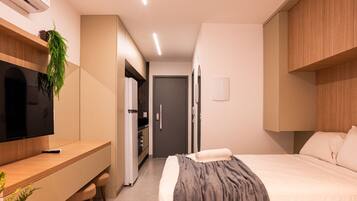 Habitación de hotel pequeña con cama, mesita de noche, televisión y un área de kitchenette.