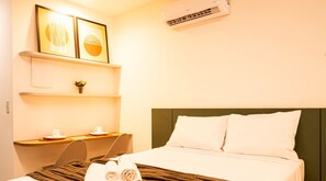 A hotel room with a bed, a desk, a chair, a shelf with a vase, and an air conditioning unit. - Simple Smart - LikeHome Hospedagens (João Pessoa)