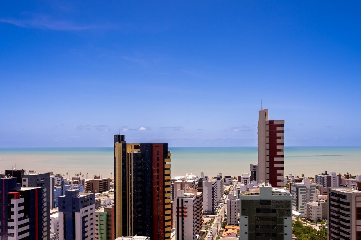Un paisaje urbano costero con rascacielos, cielo azul despejado y una playa al fondo.
