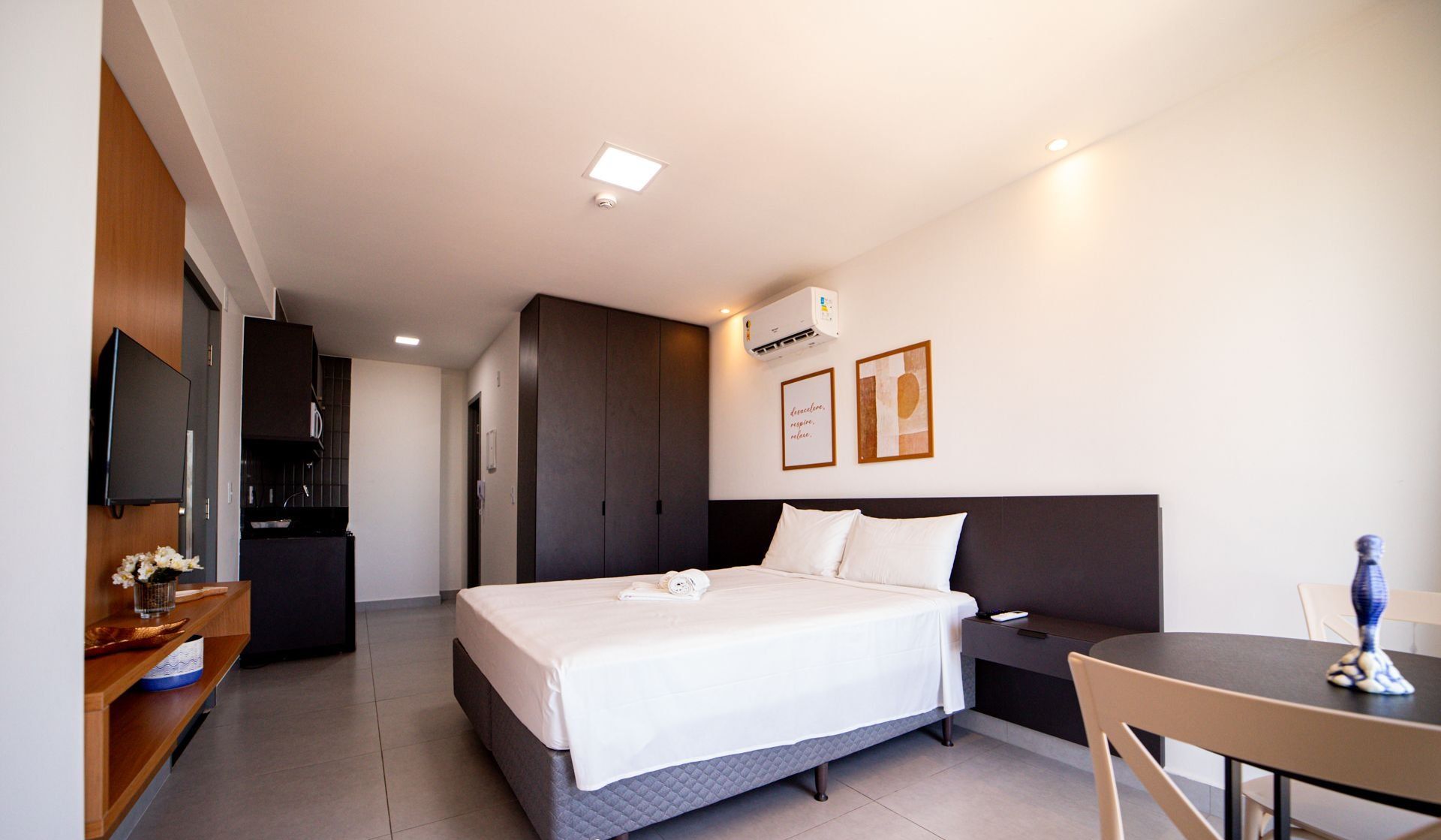Una habitación de hotel con cama, mesita de noche, televisor y una pequeña mesa de comedor.