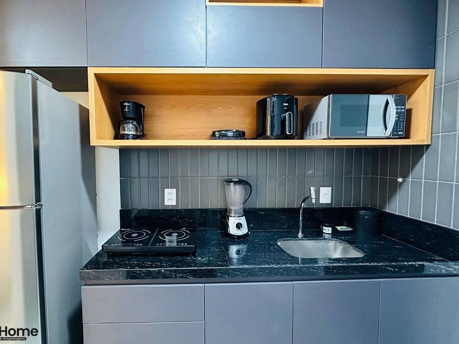 A compact kitchen with a refrigerator, a coffee maker, a microwave, a blender, and a sink.