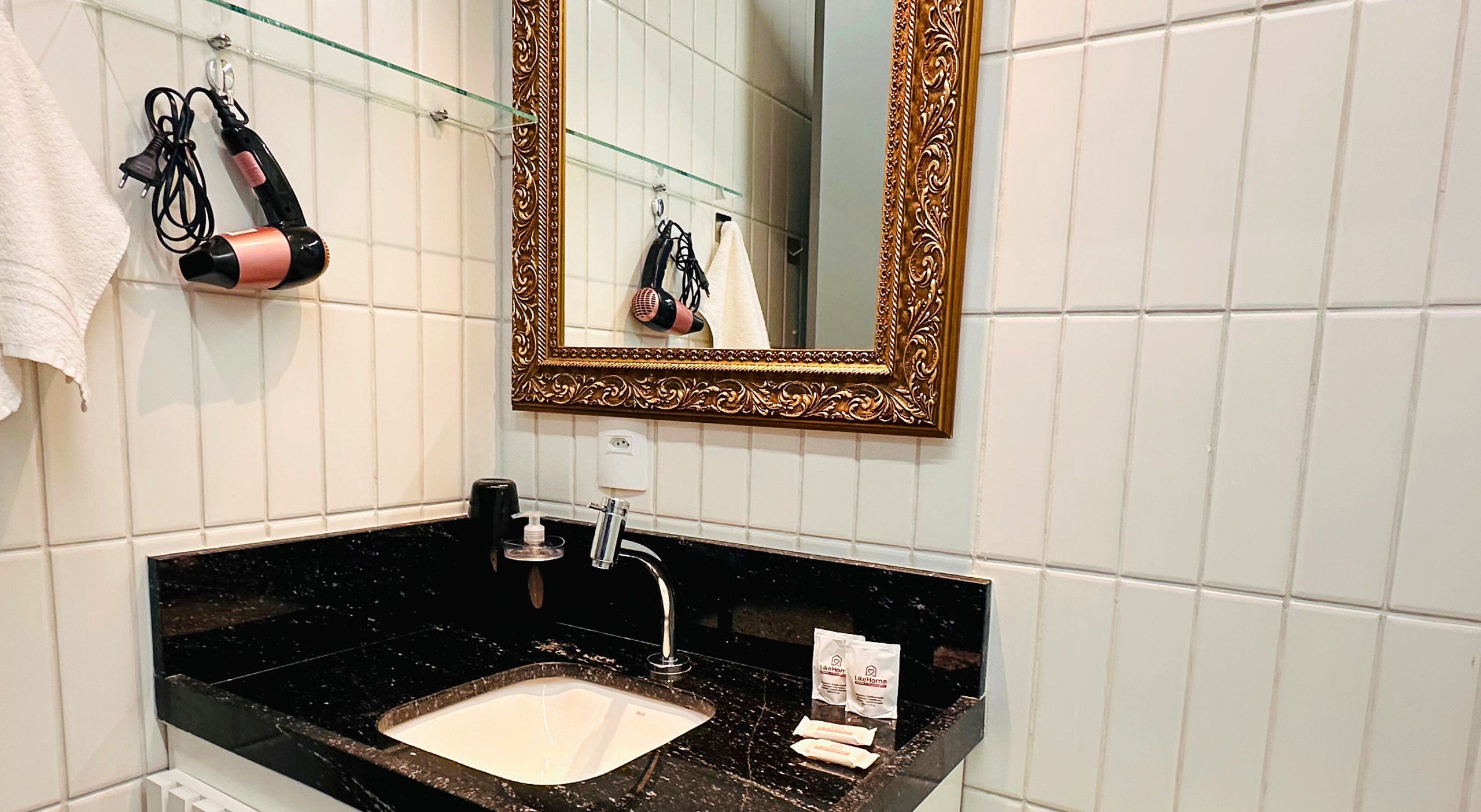 A bathroom with a black granite sink, a mirror with an ornate frame, and a towel rack with a hairdryer.