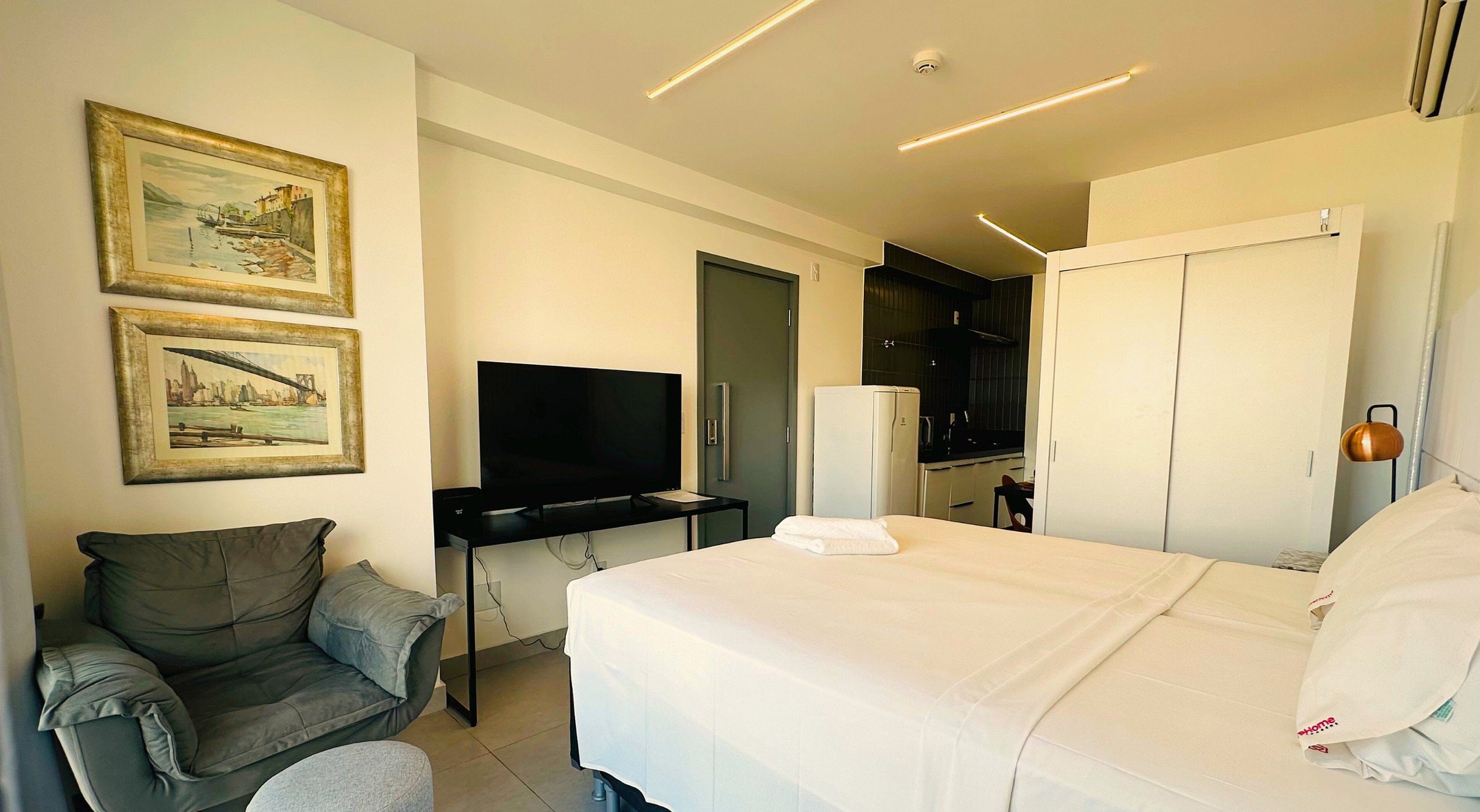 Habitación de hotel con cama, escritorio con televisor de pantalla plana, silla y dos cuadros en la pared.