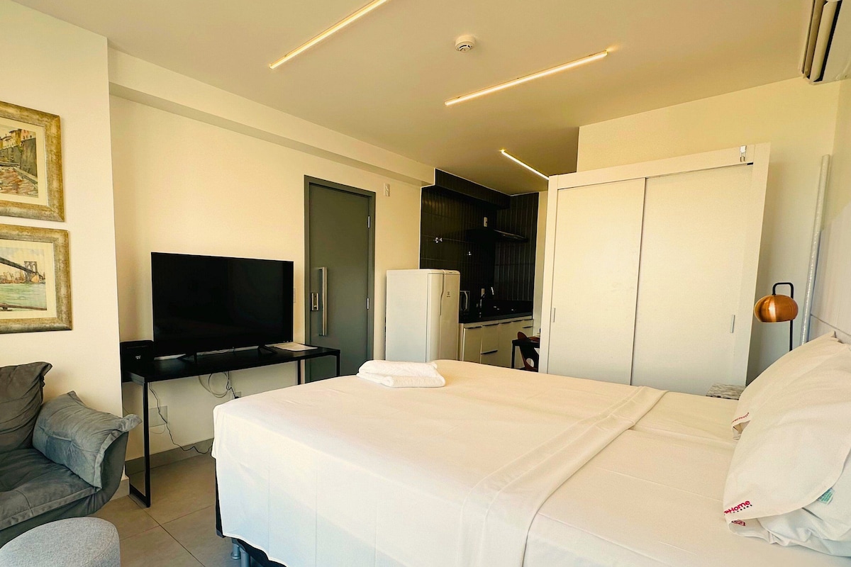 A hotel room with a bed, a desk with a flat-screen TV, a chair, and two framed pictures on the wall.