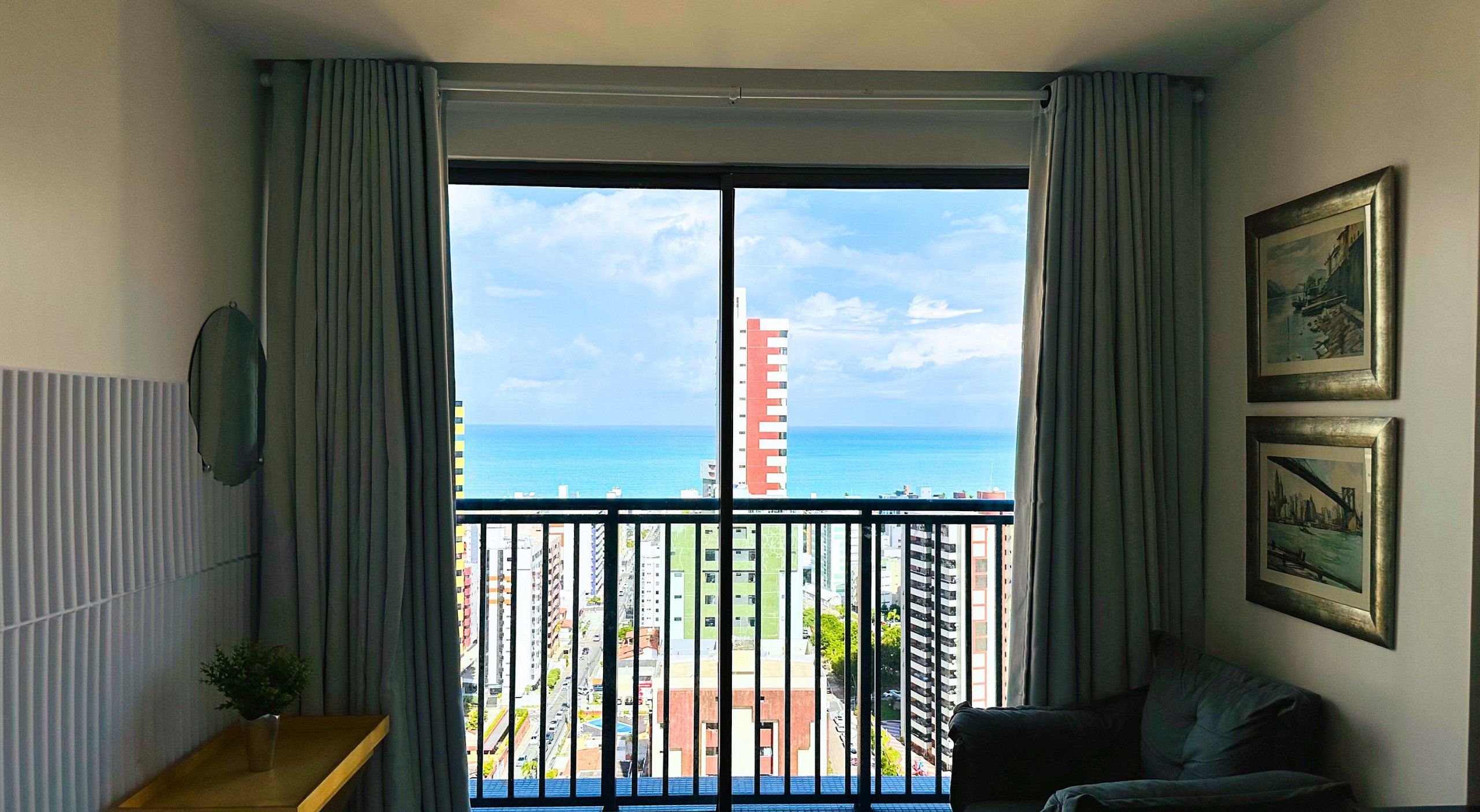 Una habitació amb un balcó, vista al mar i un edifici a la distància.