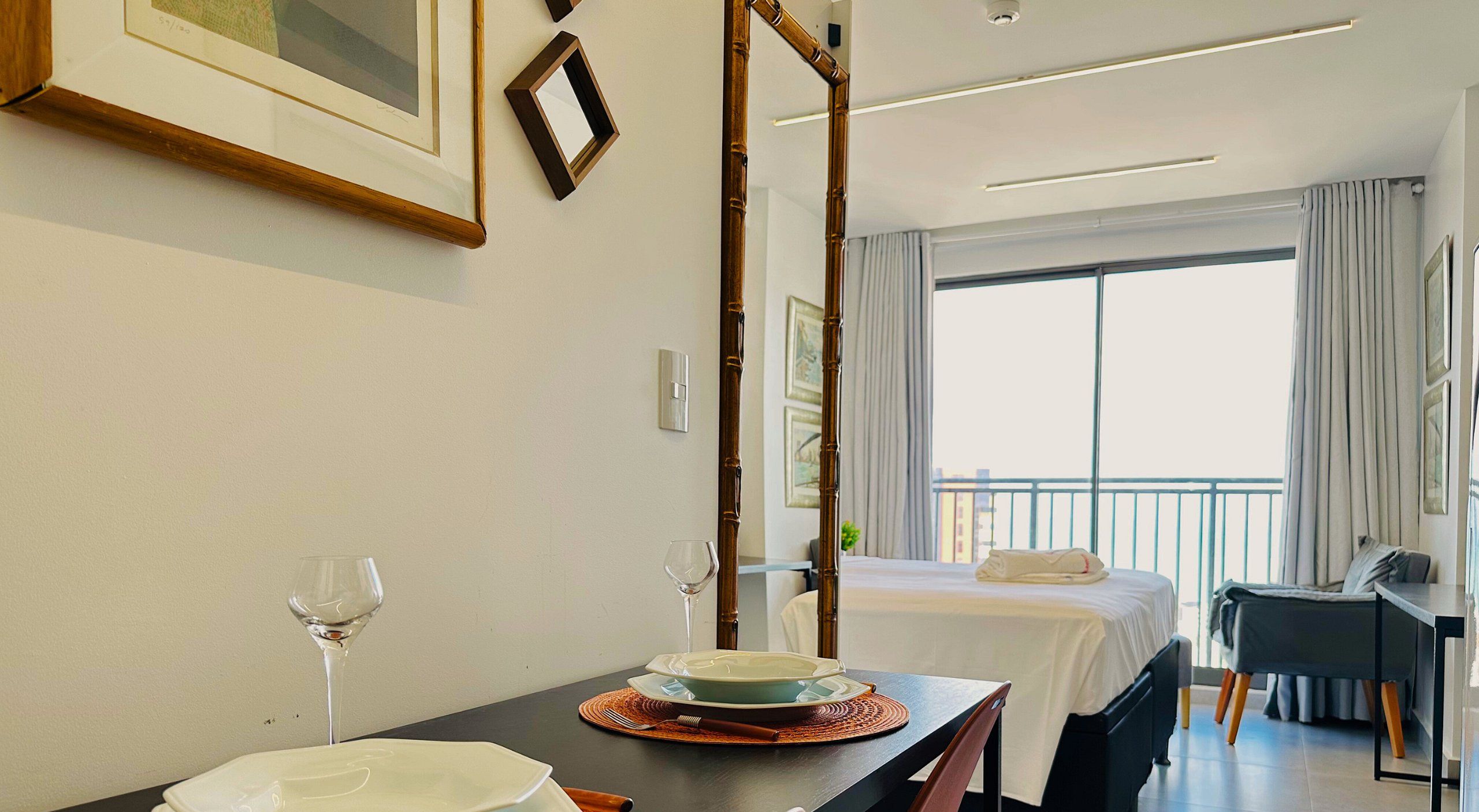 Habitación de hotel con una mesa de comedor lista para dos personas, una cama con vistas y un escritorio con una silla.