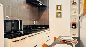 A modern kitchen with a black countertop, white cabinets, and a built-in microwave. - Simple Smart - LikeHome Hospedagens (João Pessoa)