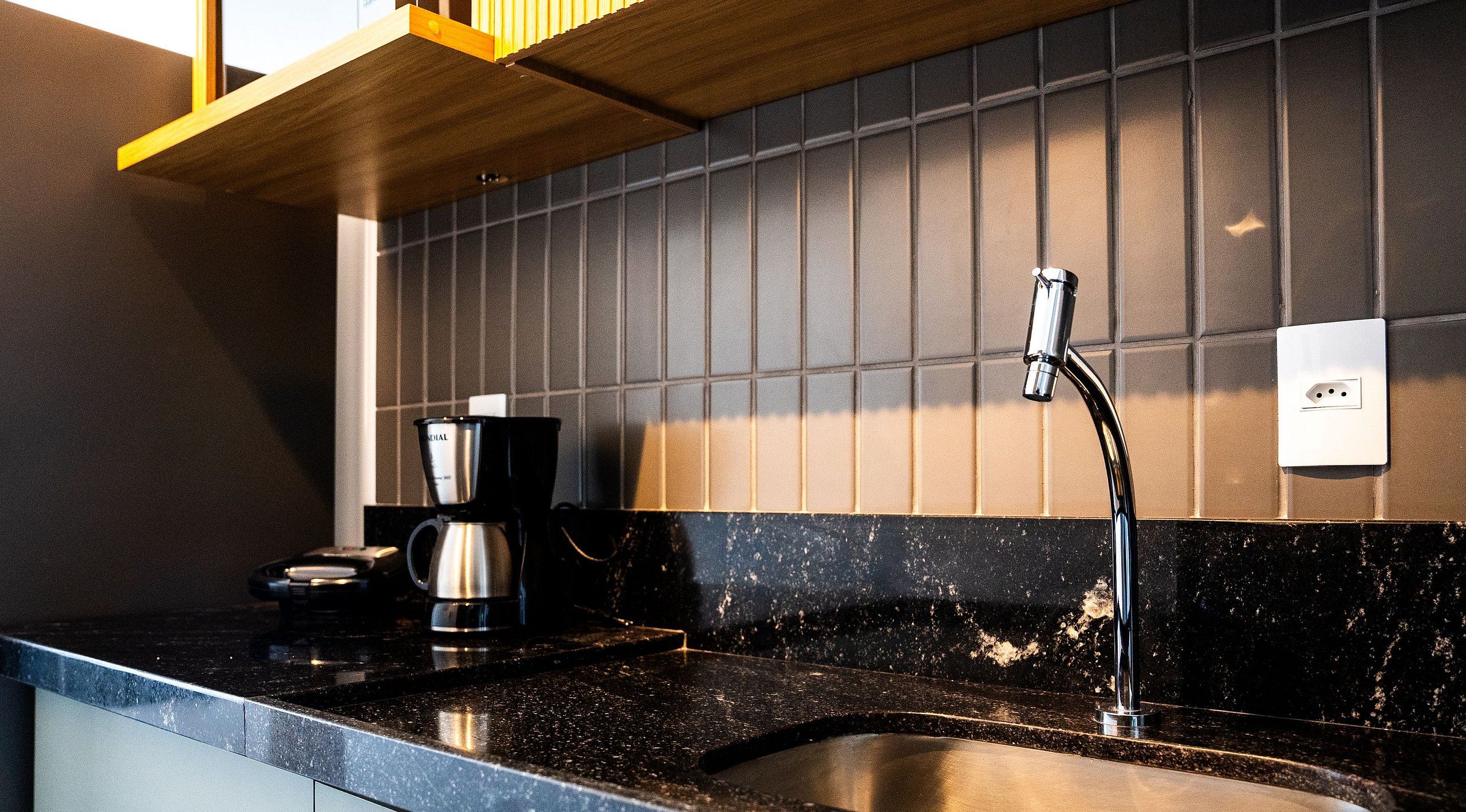 A kitchen with a black countertop, a coffee maker, and a stainless steel kettle.
