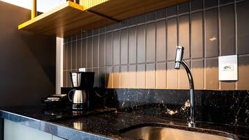 A kitchen with a black countertop, a coffee maker, and a stainless steel kettle.