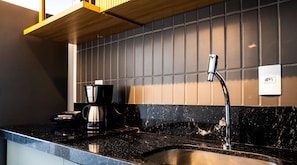 Una cocina con encimera negra, cafetera y tetera de acero inoxidable.