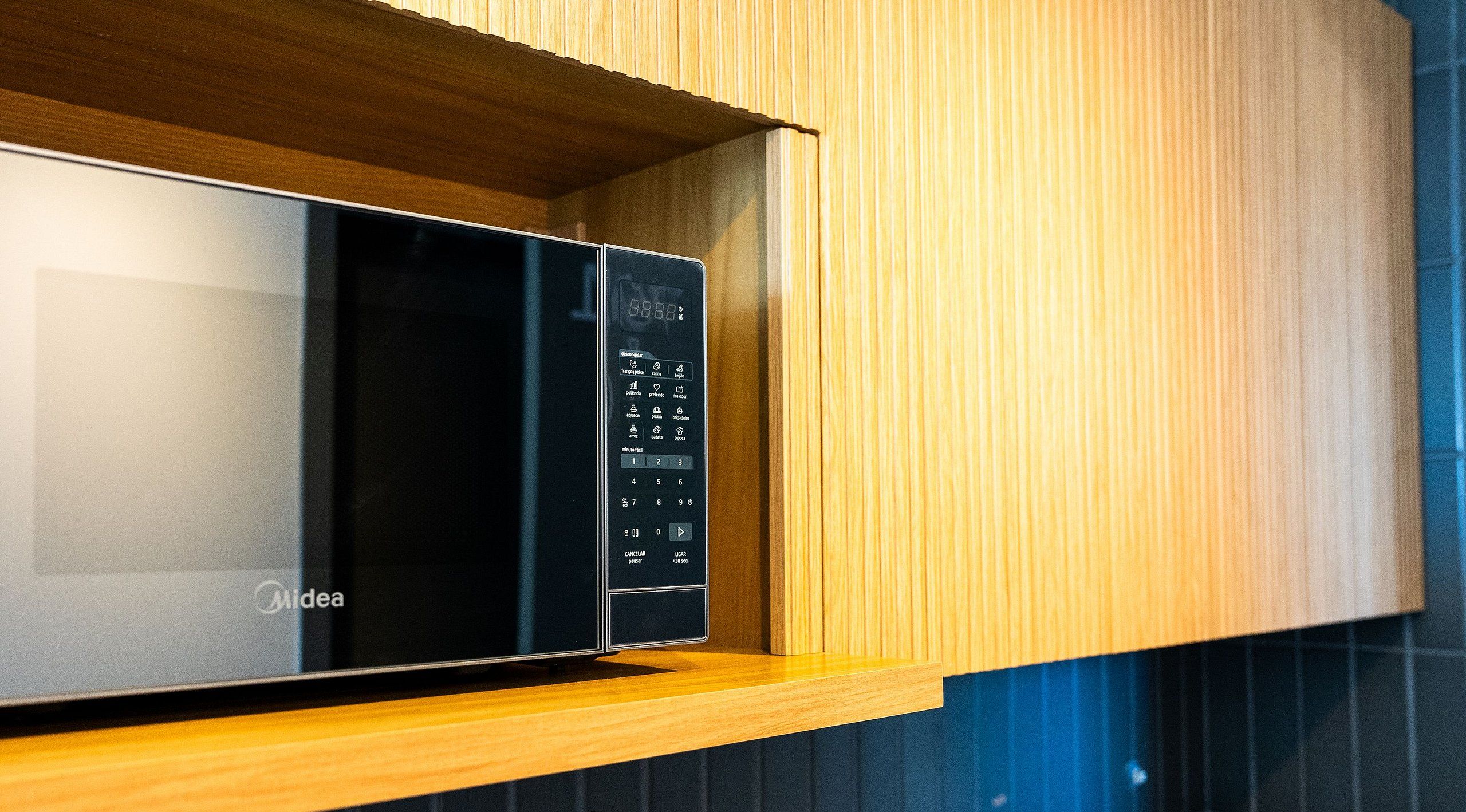 Un four à micro-ondes doté d’un écran numérique et d’un panneau de commande, placé sur une étagère en bois dans une cuisine.
