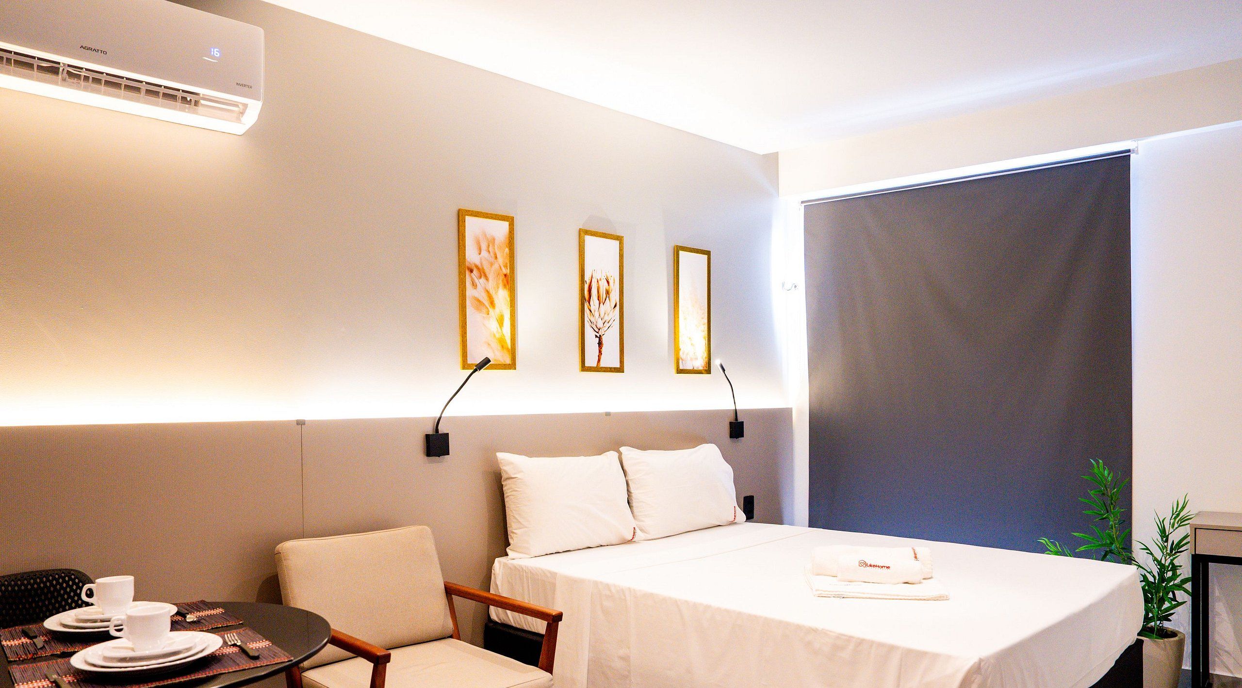 Una habitación de hotel con una cama, una mesita con una taza y plato, una silla y una planta.