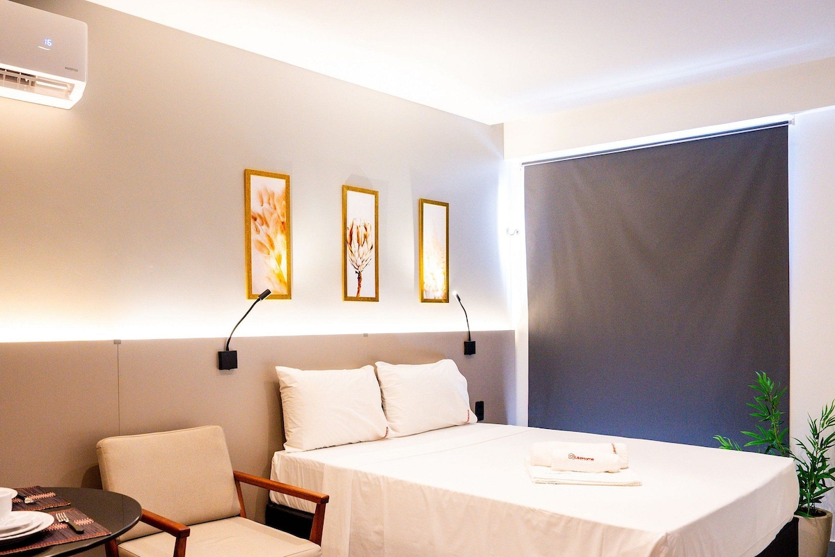 A hotel room with a bed, a small table with a cup and saucer, a chair, and a plant.