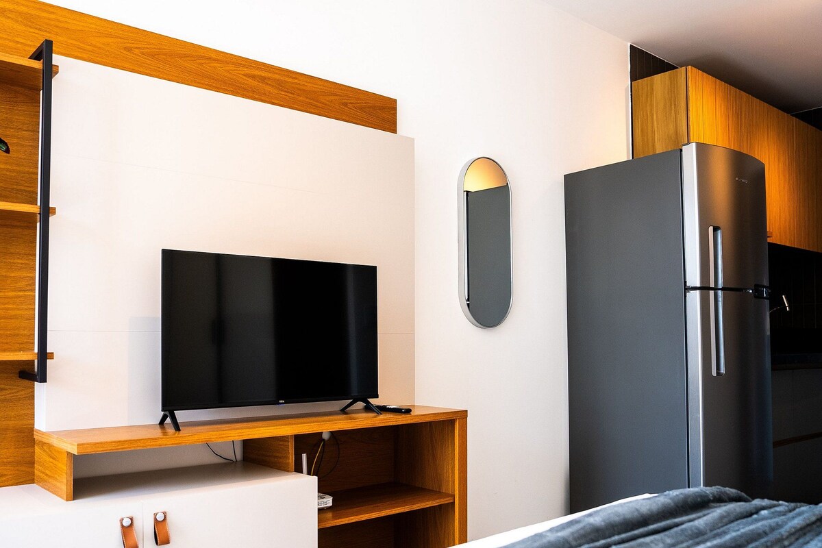 Ein modernes Zimmer mit Fernseher an einer Holzablage, einer kleinen Topfpflanze, einem Spiegel und einem eingebauten Kühlschrank.