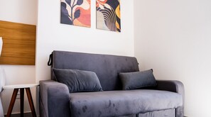 En grå soffa med två kuddar, ett vitt bord med en träbas och abstrakt konst på väggen.