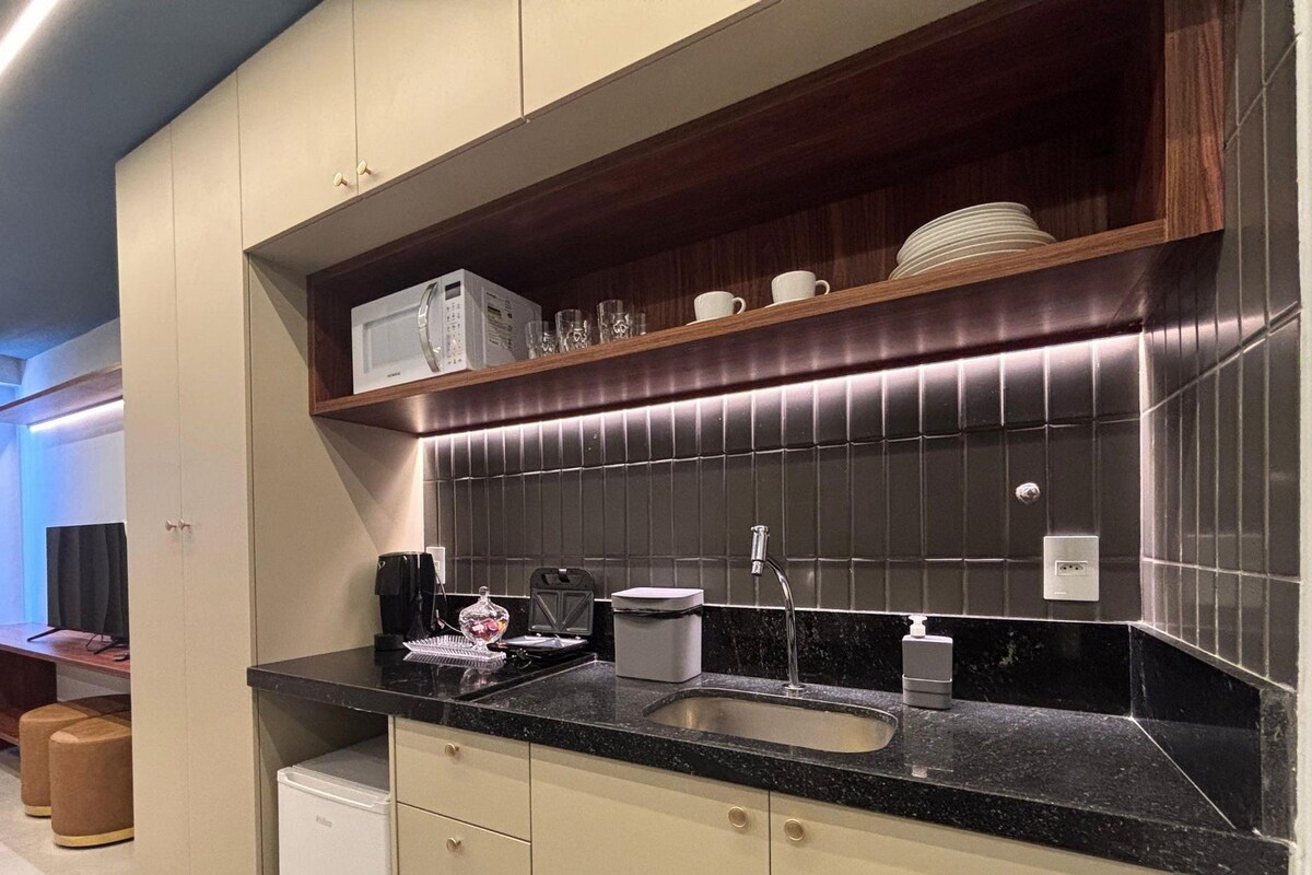 Una cocina moderna con encimera negra, pileta de acero inoxidable y microondas en la alacena.