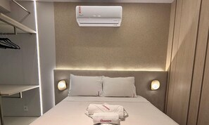 A hotel room with a bed, two bedside lamps, an air conditioning unit, and a folded towel on the bed. - Simple Smart - LikeHome Hospedagens (João Pessoa)