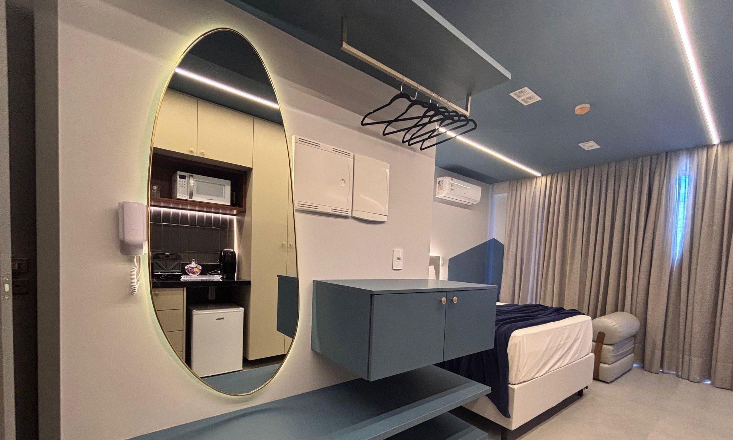 A modern bedroom with a large mirror, a bed, a desk, and a kitchenette.