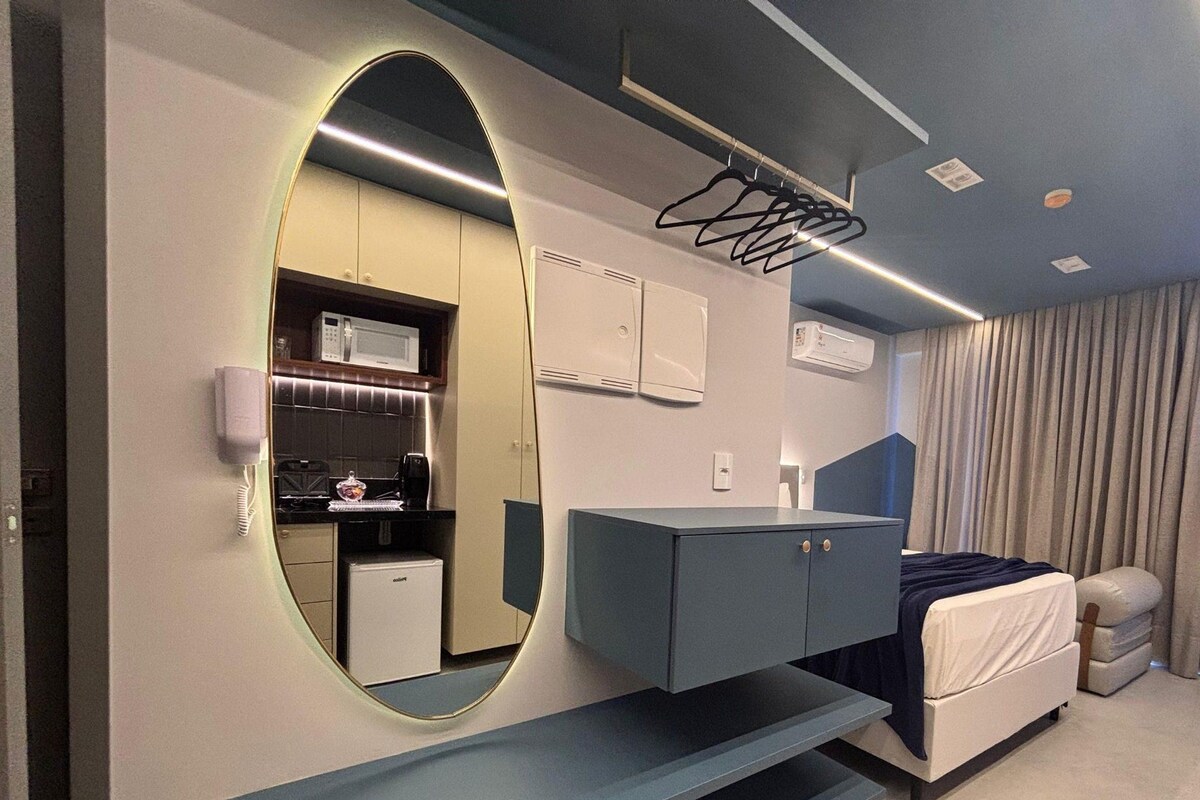 A modern bedroom with a large mirror, a bed, a desk, and a kitchenette.