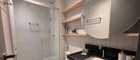 A modern bathroom with a glass-enclosed shower, a white toilet, a black sink, and a large mirror.