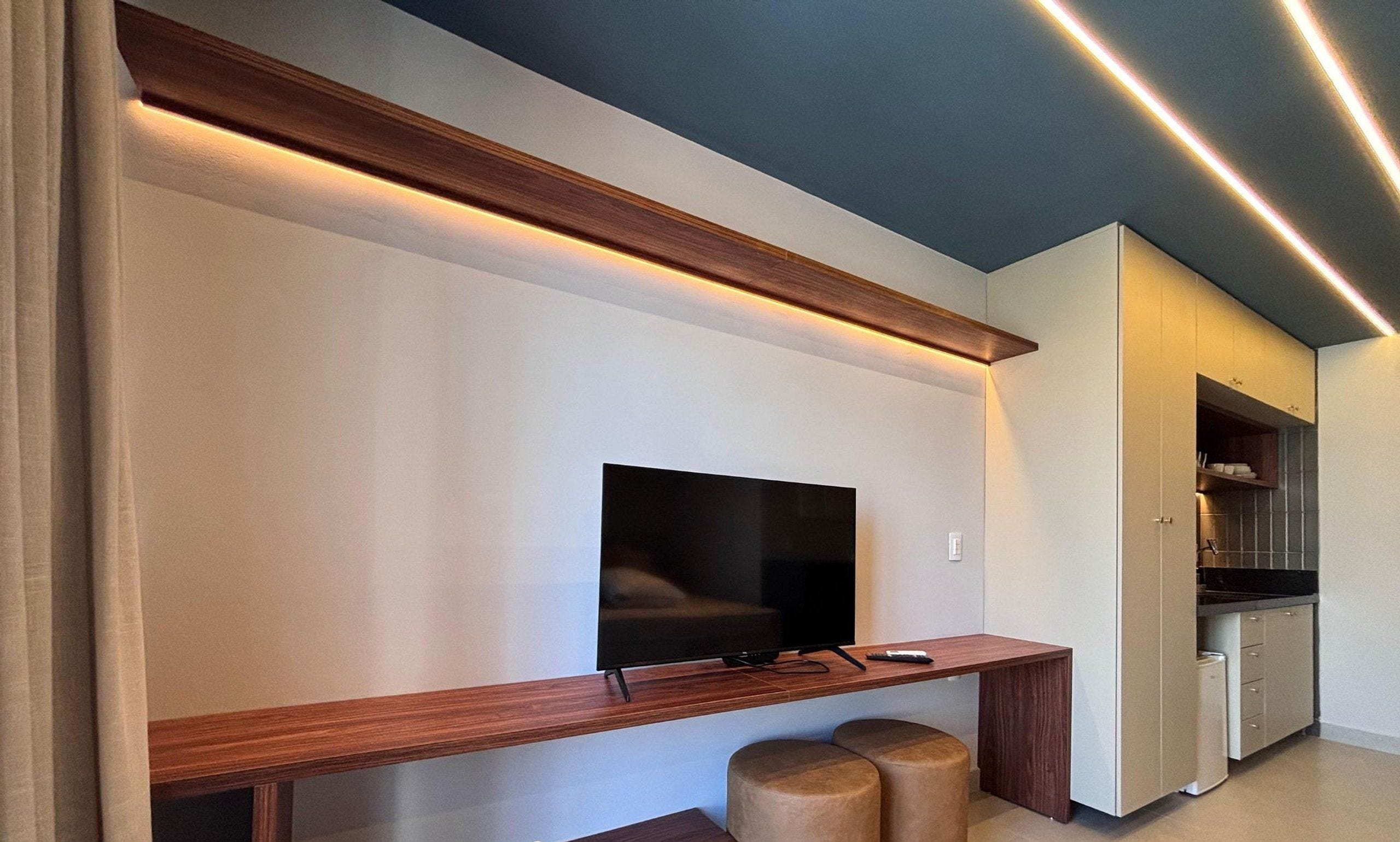 Un espacio habitable moderno con una televisión de pantalla plana montada en la pared, una mesa consola de madera y dos otomanas.