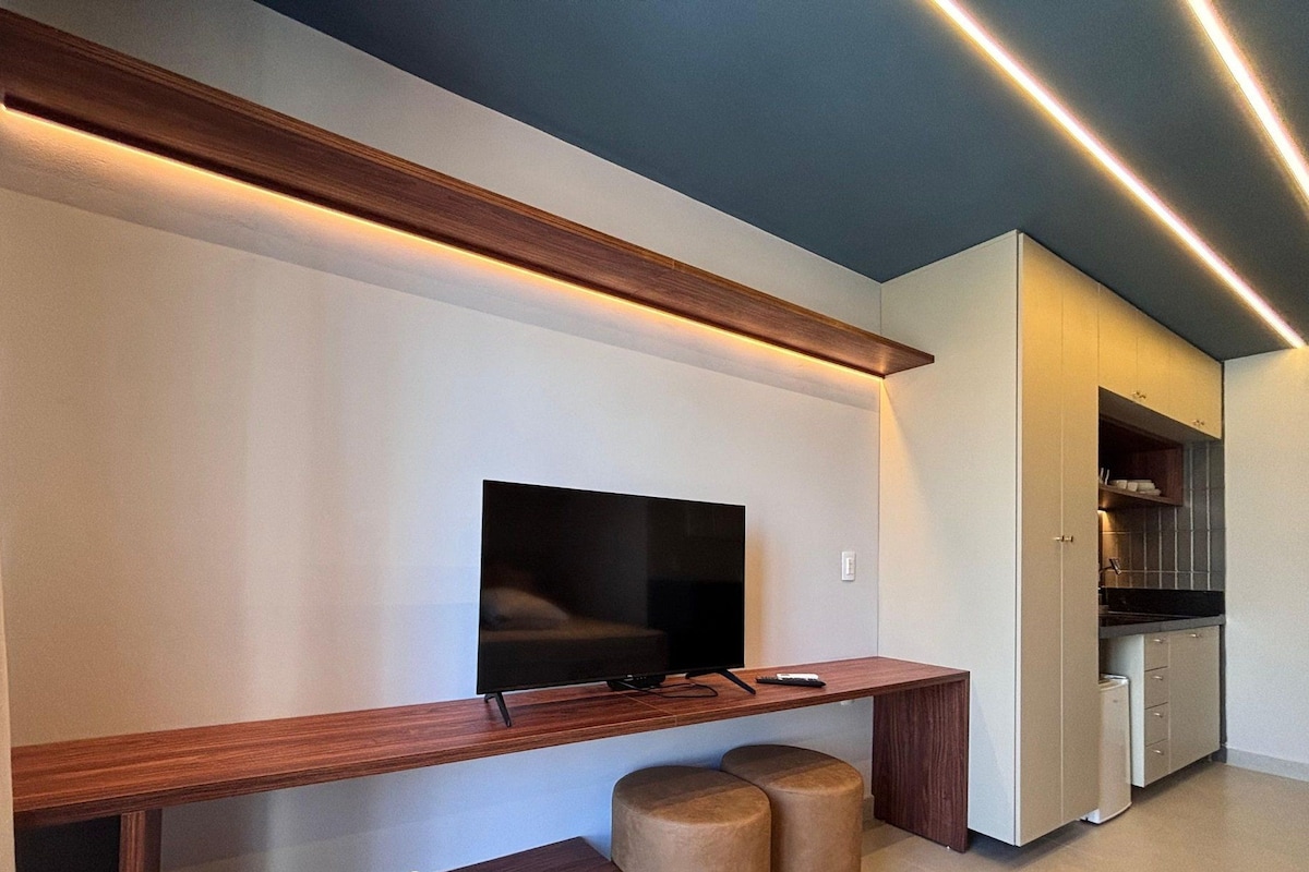 A modern living space with a flat-screen TV mounted on a wall, wooden console table, and two ottomans.