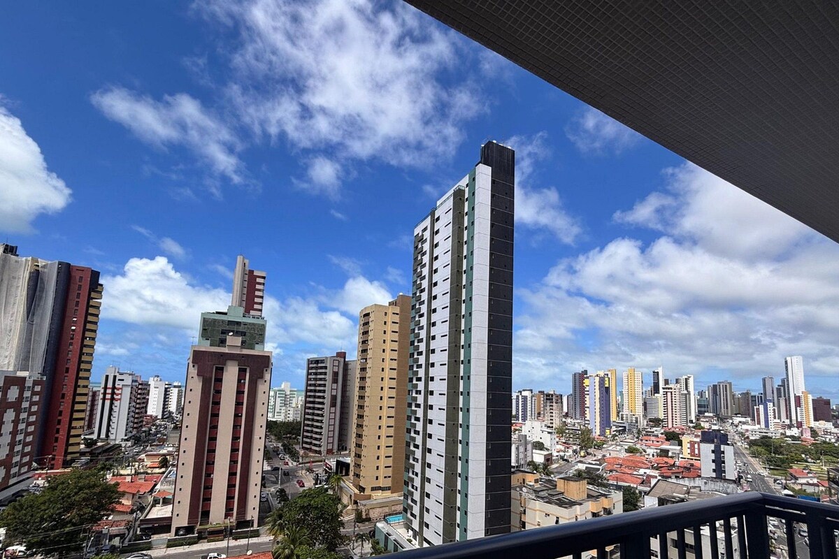 Un paisaje urbano con varios edificios altos, cielo despejado y barandilla de balcón.