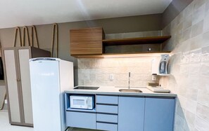 A compact kitchen with a refrigerator, microwave, sink, and wooden cabinets. - Simple Smart - LikeHome Hospedagens (João Pessoa)
