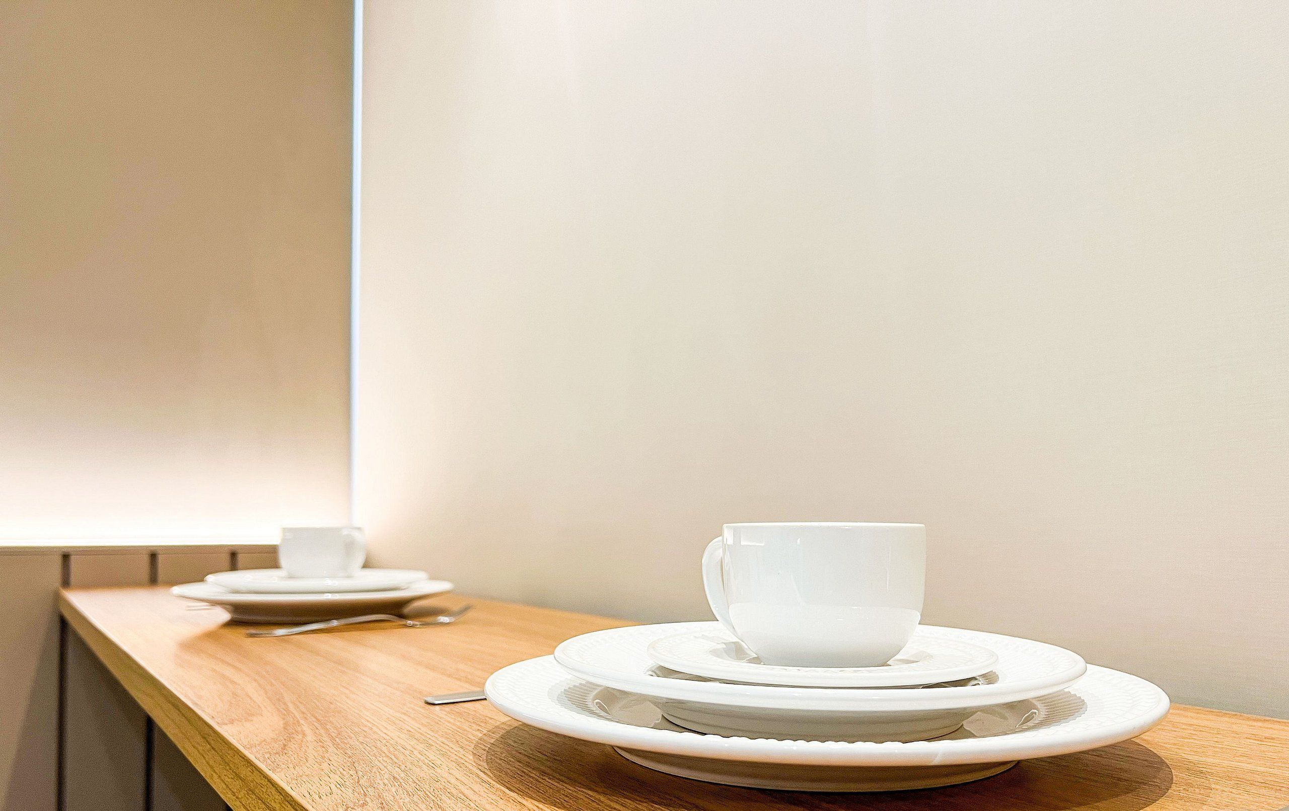 A wooden table with white plates and a cup, set against a plain wall.