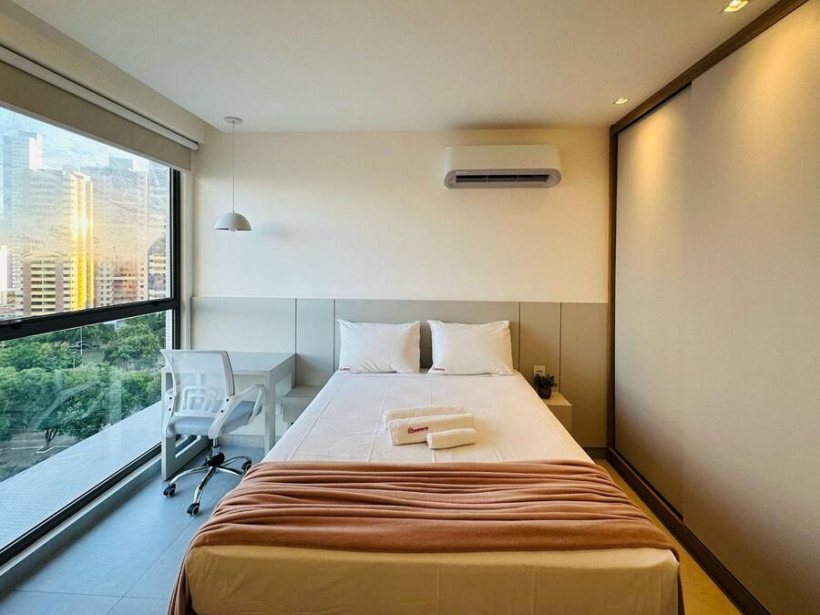 Une chambre d’hôtel avec une grande fenêtre, un lit avec du linge de lit blanc, un bureau et une chaise.
