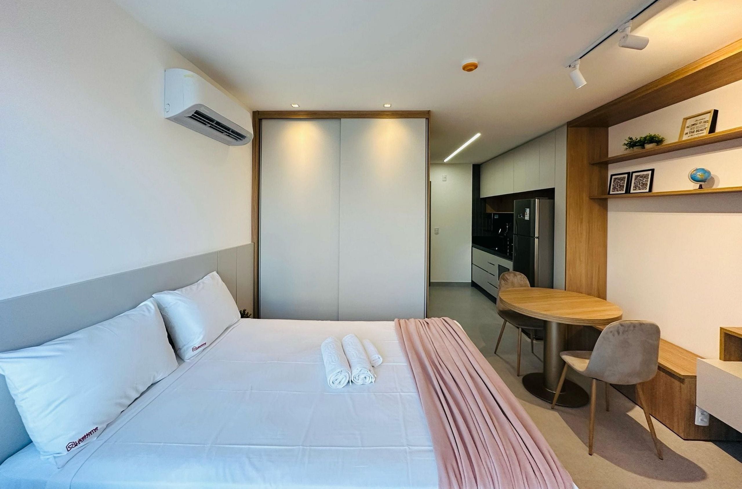 Quarto de hotel moderno com cama, escrivaninha e cozinha compacta.