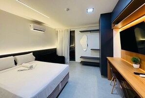 Ett hotellrum med en säng, ett skrivbord, en stol, en TV och en luftkonditioneringsanläggning.