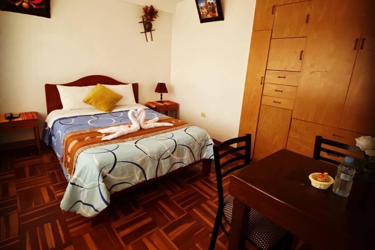 Ein Schlafzimmer mit Bett, Nachttisch, Lampe, Holzschrank und einer Essecke mit Tisch und Stühlen.