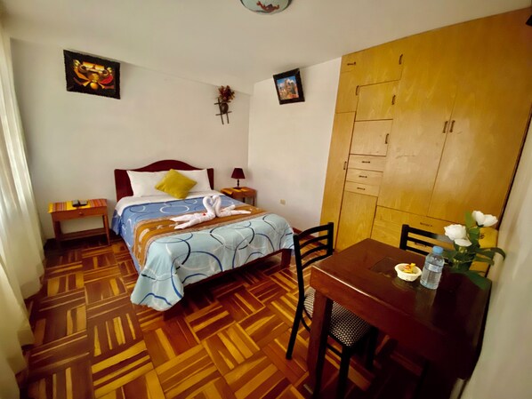 A bedroom with a bed, a wooden wardrobe, a dining table with chairs, and a small table with a vase of flowers. - Amira's House Cusco (Cusco)