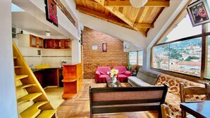 A spacious living area with a wooden staircase, a brick wall, and a large window offering a city view. - Amira's House Cusco (Cusco)