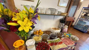 A buffet table with various food items, a vase of flowers, and a coffee machine. - Amira's House Cusco (Cusco)