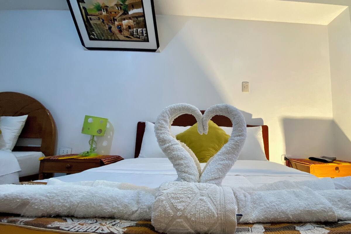 Ein Hotelzimmer mit einem Bett, einer herzförmigen Handtuchgestaltung, einer grünen Lampe und einem gerahmten Bild an der Wand.