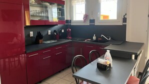 Una cocina compacta con armarios rojos, encimera negra y una zona de comedor con mesa y sillas.