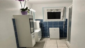 Una cocina compacta con armarios blancos, una ventana pequeña y paredes con azulejos azules.