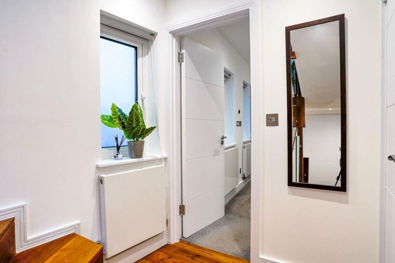 Een gang met een bloempot, een radiator en een spiegel aan de muur.