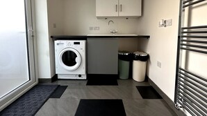 A compact kitchen with a washing machine, a small fridge, and two trash bins.