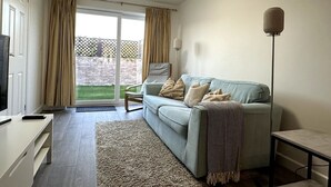 A modern living room with a sofa, a coffee table, a TV, and a lamp. There is a sliding glass door leading to a balcony.