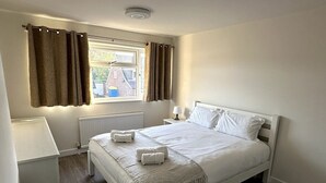 A neatly arranged bedroom with a bed, bedside tables, and a window with curtains.
