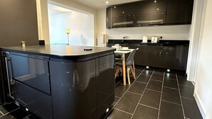 A modern kitchen with dark cabinetry, a central island, and a dining area with a table and chairs.